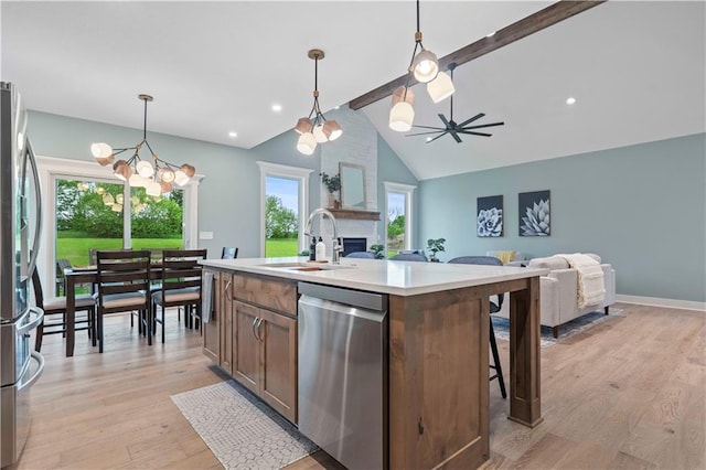 kitchen with sink, light hardwood / wood-style flooring, stainless steel appliances, a center island with sink, and decorative light fixtures