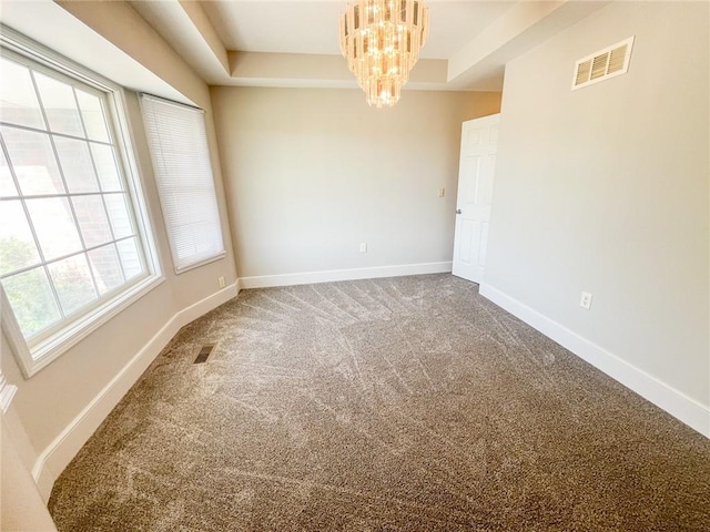 carpeted empty room with a notable chandelier and a tray ceiling