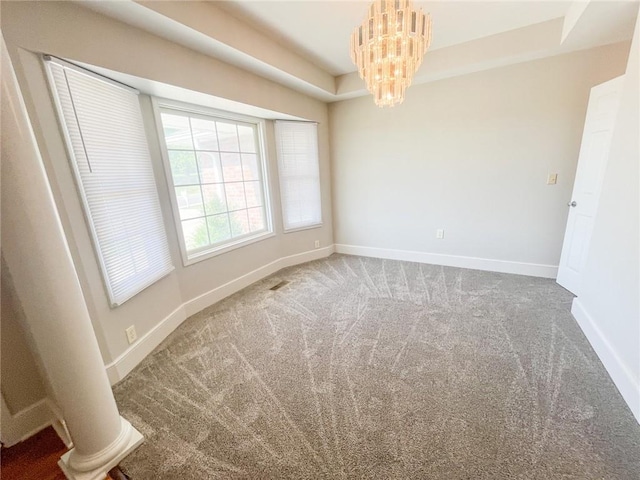 carpeted empty room with a tray ceiling, a chandelier, and ornate columns