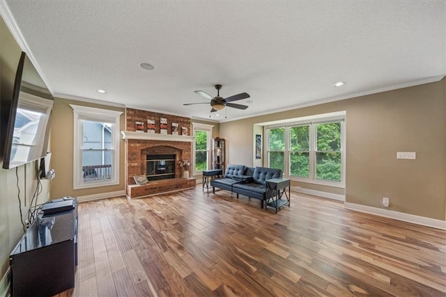 unfurnished living room with brick wall, a fireplace, ceiling fan, hardwood / wood-style flooring, and crown molding