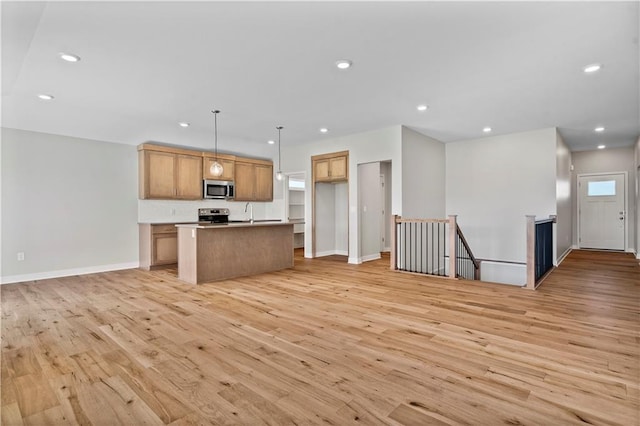 kitchen with plenty of natural light, a kitchen island with sink, light hardwood / wood-style flooring, appliances with stainless steel finishes, and decorative light fixtures