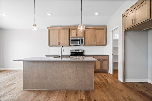 kitchen featuring a center island with sink, light hardwood / wood-style floors, stainless steel appliances, and hanging light fixtures