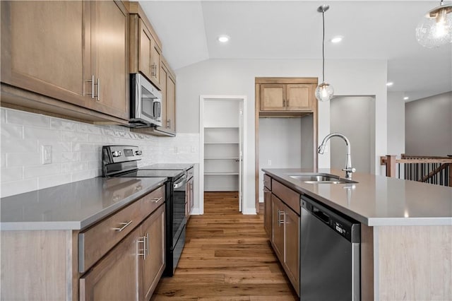 kitchen with a kitchen island with sink, hanging light fixtures, vaulted ceiling, light wood-type flooring, and appliances with stainless steel finishes