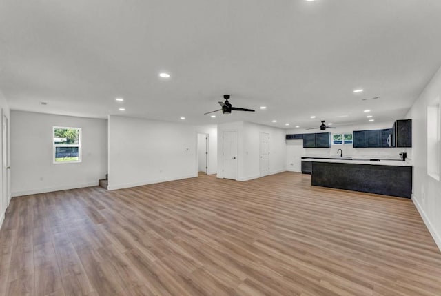 unfurnished living room with sink, ceiling fan, and light wood-type flooring