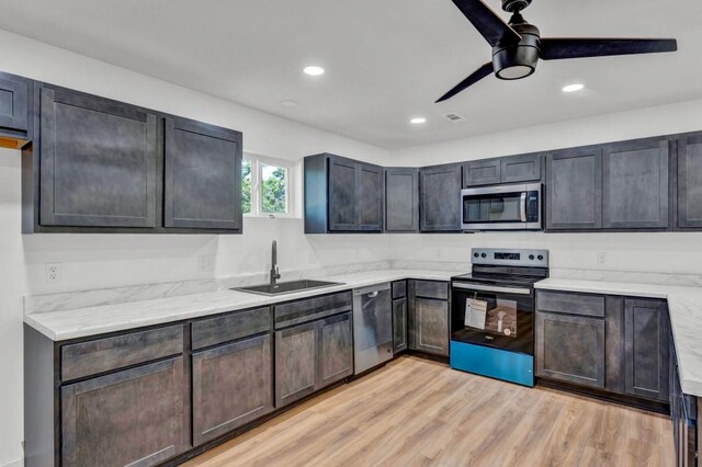 kitchen with ceiling fan, light wood-type flooring, light stone counters, sink, and appliances with stainless steel finishes