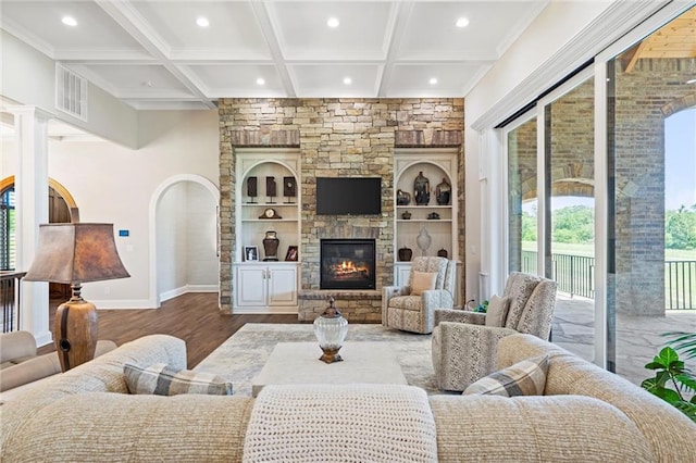 living room featuring a stone fireplace, wood-type flooring, a wealth of natural light, and coffered ceiling