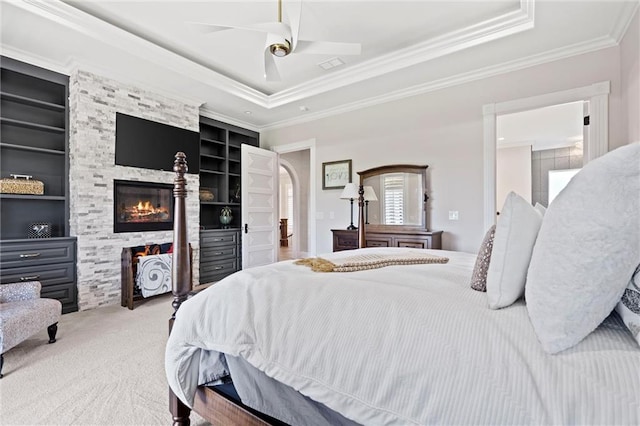 carpeted bedroom featuring a fireplace, a raised ceiling, ceiling fan, and ornamental molding