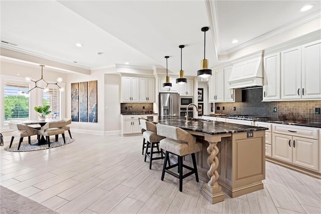 kitchen with appliances with stainless steel finishes, white cabinetry, a kitchen island with sink, and dark stone counters