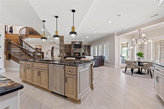 kitchen featuring dishwasher, sink, an inviting chandelier, dark stone countertops, and a kitchen island with sink