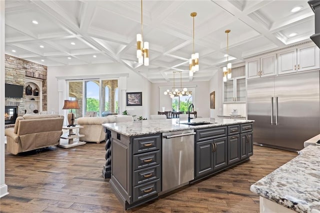 kitchen with an island with sink, glass insert cabinets, open floor plan, light stone countertops, and stainless steel appliances