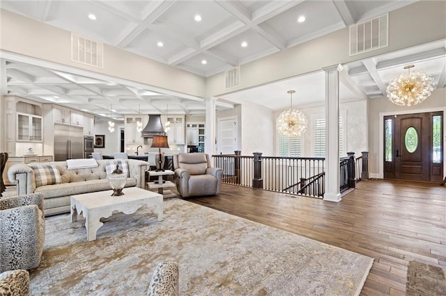 living area with an inviting chandelier, visible vents, wood finished floors, and ornate columns