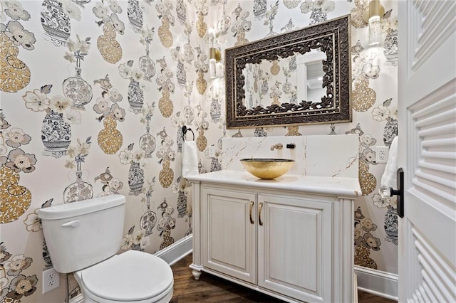 half bathroom with toilet, wallpapered walls, baseboards, and vanity