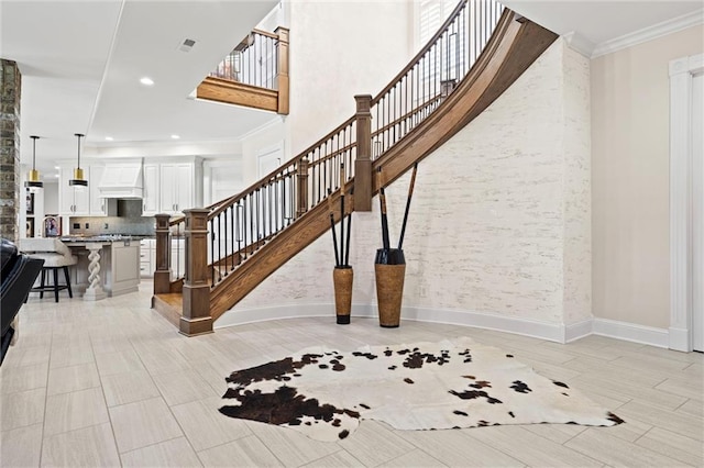 stairs with baseboards, visible vents, a towering ceiling, ornamental molding, and recessed lighting