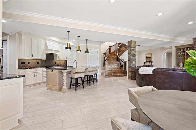 kitchen with open floor plan, backsplash, an island with sink, dark countertops, and pendant lighting