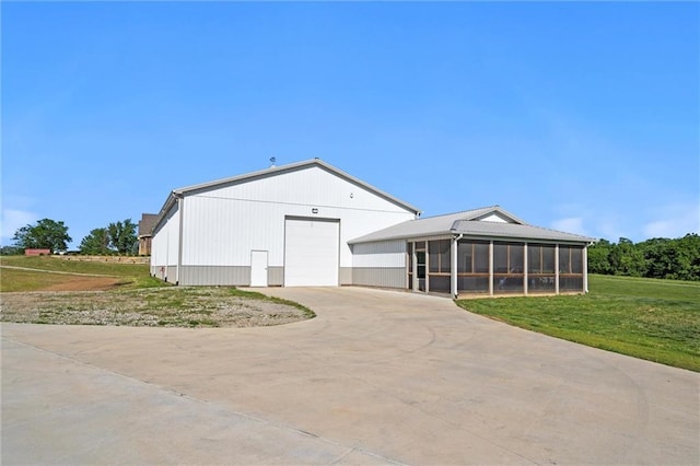 view of front of home featuring driveway, a front lawn, a detached garage, and a sunroom