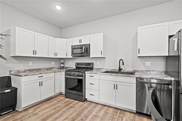 kitchen with appliances with stainless steel finishes, light wood-style flooring, a sink, and white cabinetry