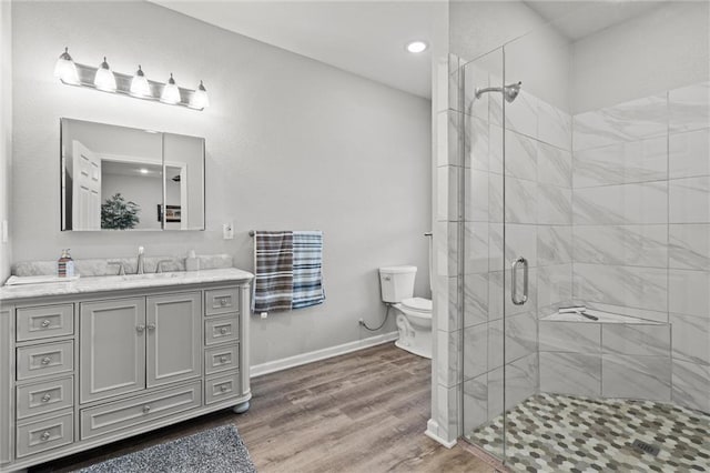 bathroom with toilet, wood finished floors, vanity, baseboards, and a stall shower