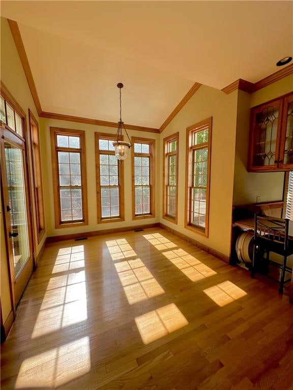 dining space featuring vaulted ceiling, plenty of natural light, ornamental molding, and hardwood / wood-style flooring