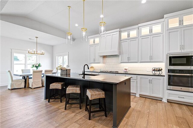 24932 W 98th Pl, Lenexa, KS 66227 - kitchen with stainless steel appliances, a sink, custom range hood, a kitchen breakfast bar, and light wood-style flooring