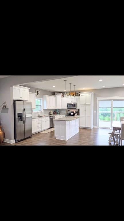 kitchen with decorative light fixtures, white cabinetry, sink, a center island, and stainless steel appliances