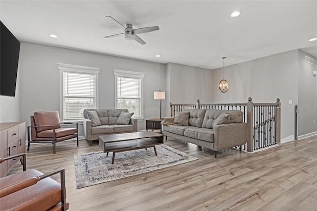 living room with ceiling fan with notable chandelier and light hardwood / wood-style floors