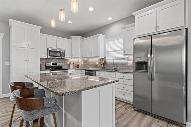 kitchen featuring pendant lighting, dark stone countertops, stainless steel appliances, a kitchen breakfast bar, and white cabinets