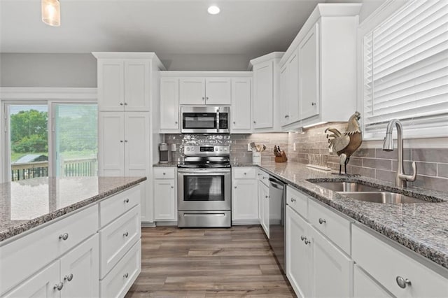 kitchen featuring white cabinets, light stone counters, a sink, stainless steel appliances, and backsplash