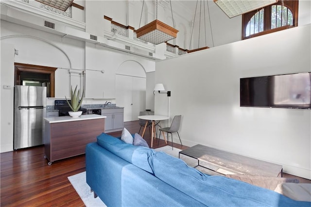 living room featuring sink, a towering ceiling, and dark wood-type flooring