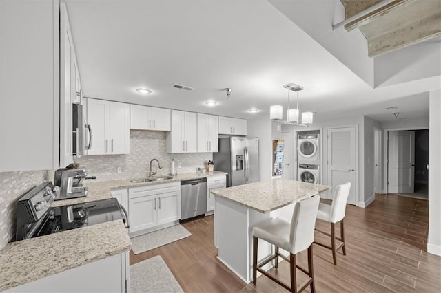 kitchen with appliances with stainless steel finishes, pendant lighting, white cabinetry, stacked washer and clothes dryer, and a kitchen island