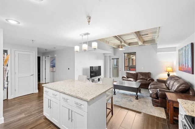 kitchen featuring a breakfast bar, hanging light fixtures, a center island, wood-type flooring, and white cabinets