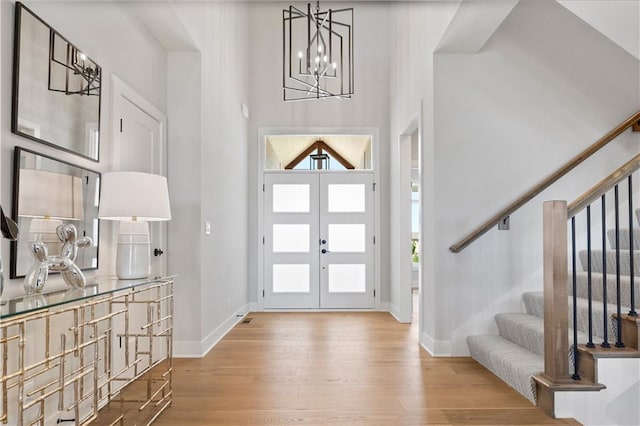 entrance foyer with french doors, wood finished floors, a chandelier, baseboards, and stairs