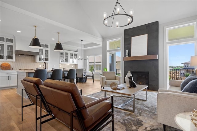 living area with lofted ceiling, recessed lighting, light wood-style flooring, a large fireplace, and a chandelier