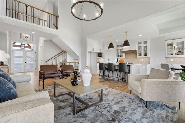 living area with stairway, french doors, light wood-style flooring, and an inviting chandelier