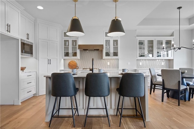 kitchen with a center island with sink, white cabinets, stainless steel microwave, light countertops, and light wood-style floors