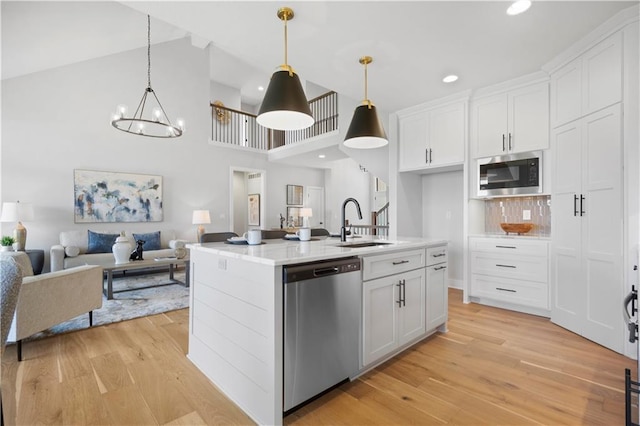 kitchen with stainless steel appliances, a sink, white cabinetry, open floor plan, and light wood-type flooring