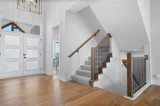 entrance foyer with baseboards, stairway, wood finished floors, vaulted ceiling, and a chandelier