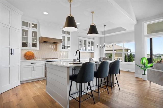 kitchen with an island with sink, light wood-style floors, custom range hood, and a sink