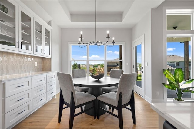 dining space featuring light wood-style floors, a tray ceiling, a healthy amount of sunlight, and an inviting chandelier