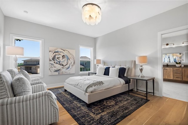 bedroom with ensuite bath, baseboards, and wood finished floors