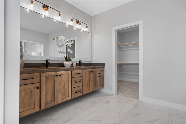 full bath with double vanity, baseboards, marble finish floor, a walk in closet, and a sink