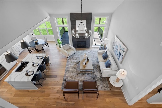 living area with baseboards, wood finished floors, vaulted ceiling, a fireplace, and a chandelier