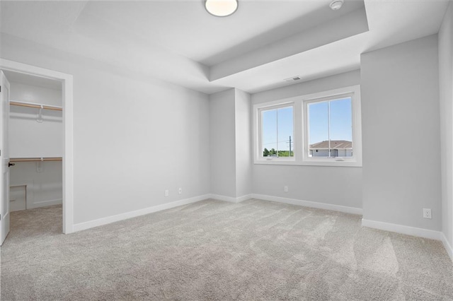 unfurnished bedroom featuring a tray ceiling, carpet, a walk in closet, and baseboards