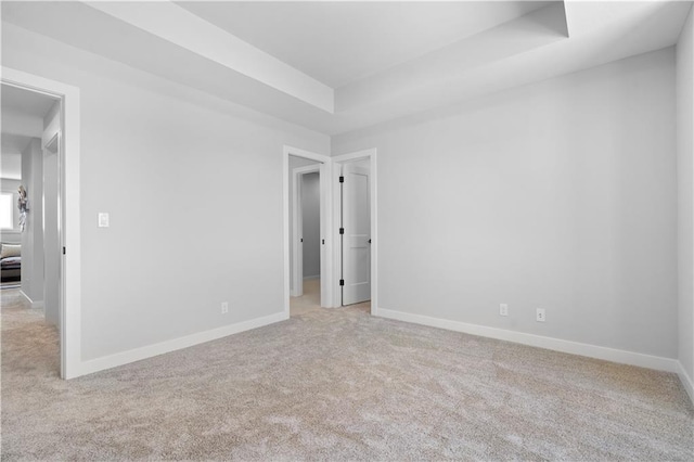 empty room with carpet flooring, a raised ceiling, and baseboards