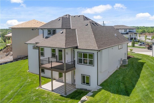 rear view of house with a shingled roof, cooling unit, a patio, and a yard