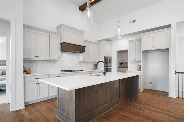 kitchen featuring a center island with sink, stainless steel appliances, wall chimney range hood, pendant lighting, and sink