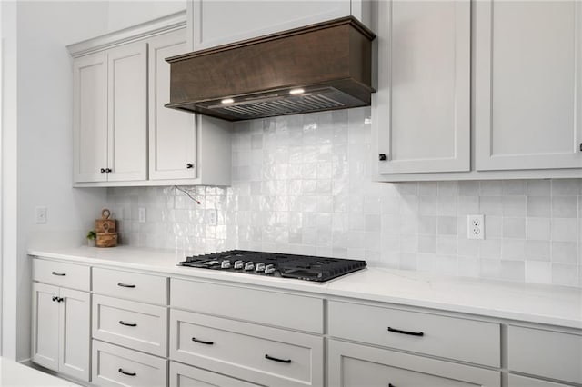 kitchen featuring white cabinetry, stainless steel gas stovetop, backsplash, light stone counters, and custom range hood