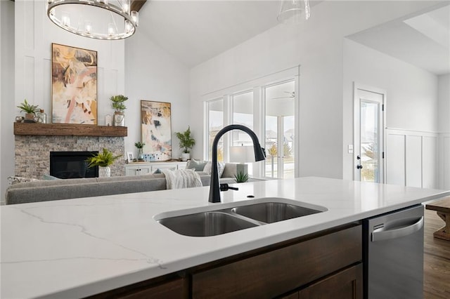 kitchen with a stone fireplace, light stone counters, stainless steel dishwasher, vaulted ceiling, and sink