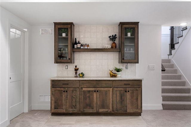 bar with tasteful backsplash, dark brown cabinets, and light colored carpet