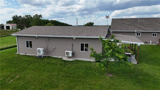 rear view of house featuring ac unit, a shingled roof, and a lawn