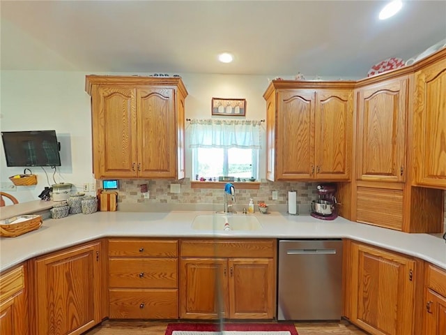 kitchen with brown cabinetry, dishwasher, backsplash, light countertops, and a sink